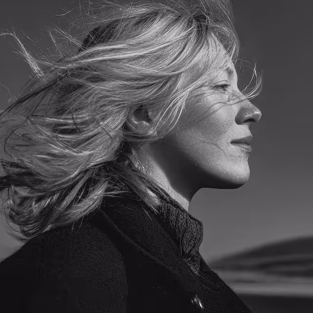Black and white profile of a blonde woman with windblown hair looking peacefully to the right.