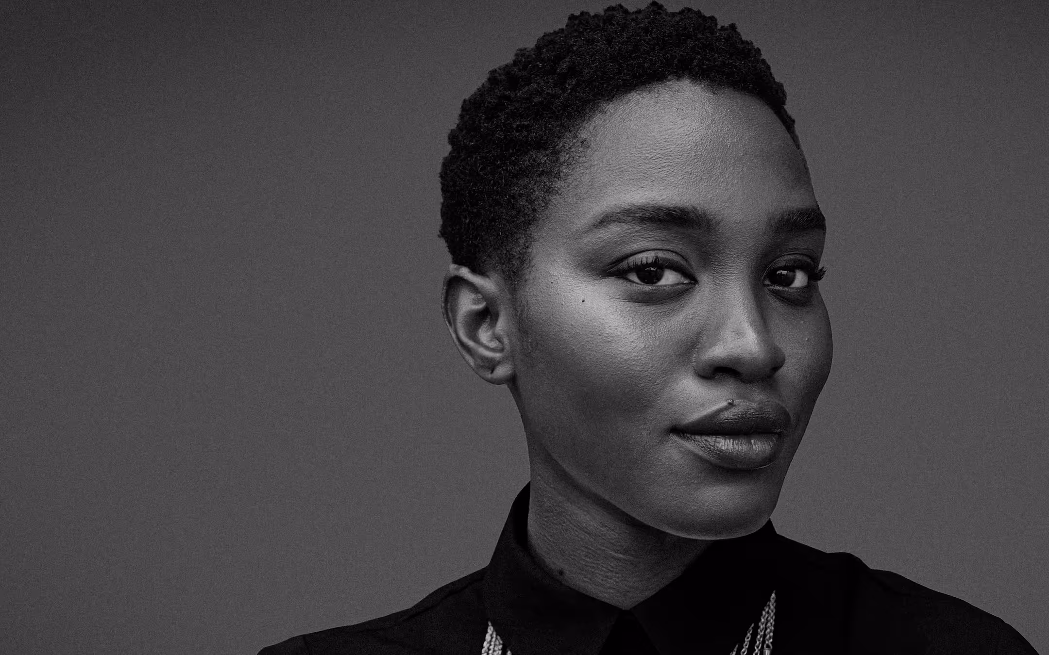 Black and white close-up portrait of a confident woman with short curly hair wearing a dark collared shirt.