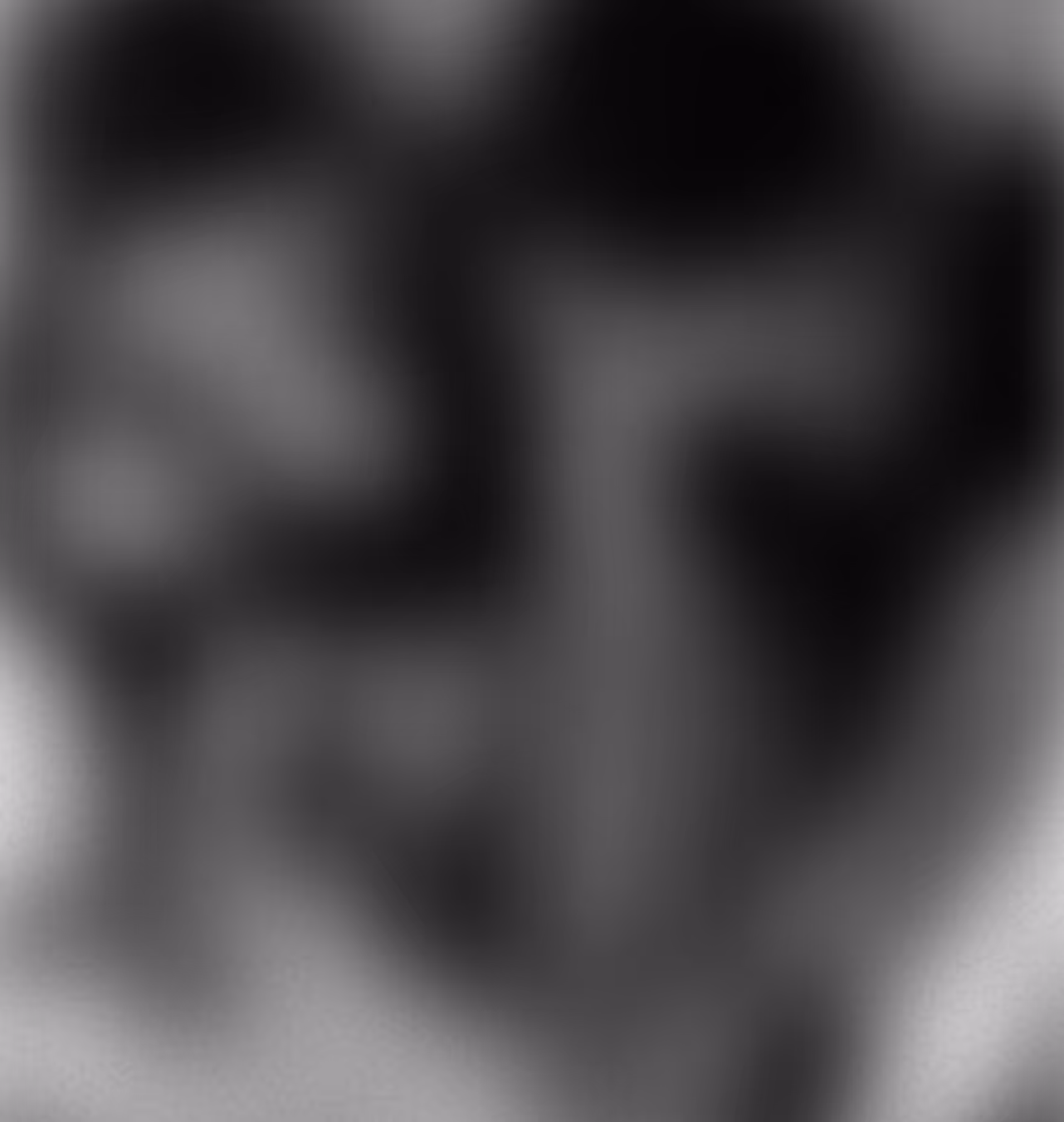 Black and white close-up portrait of a man with mustache and goatee looking down.