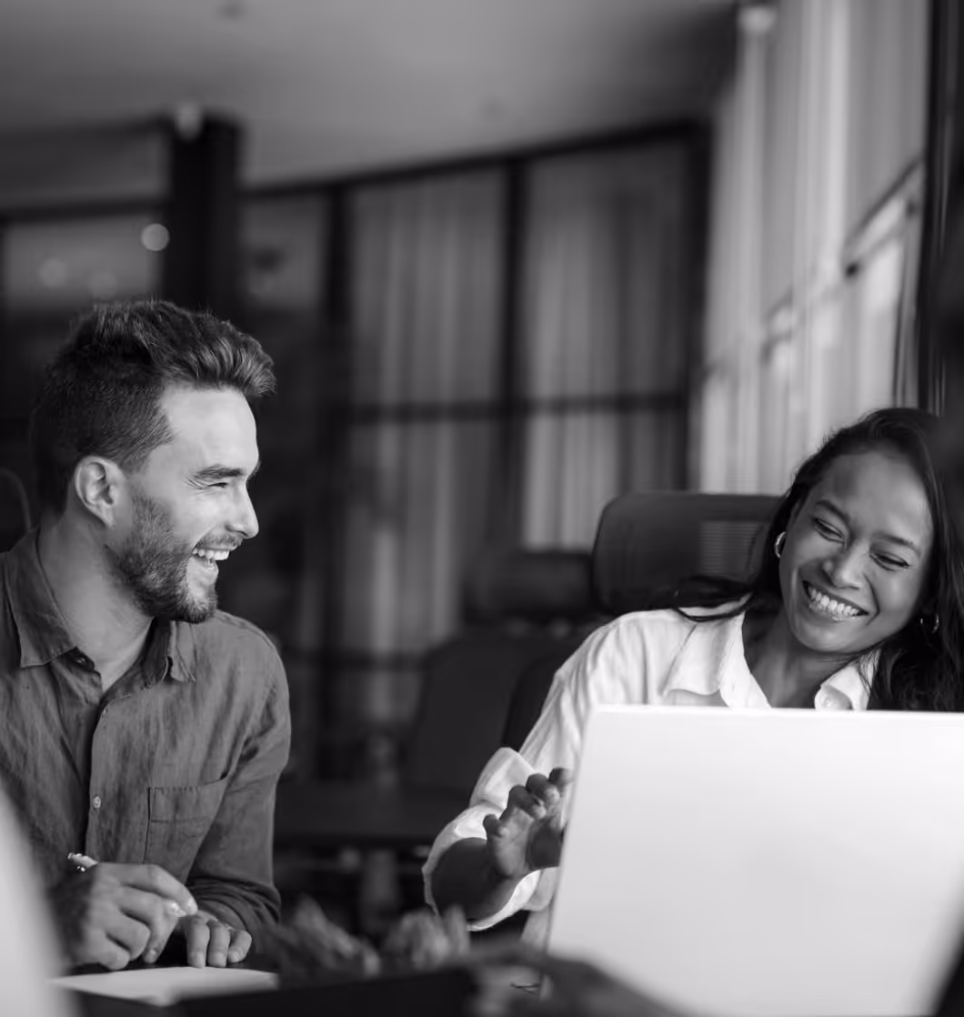 Smiling man and woman collaborating in an office, woman pointing at a laptop screen.