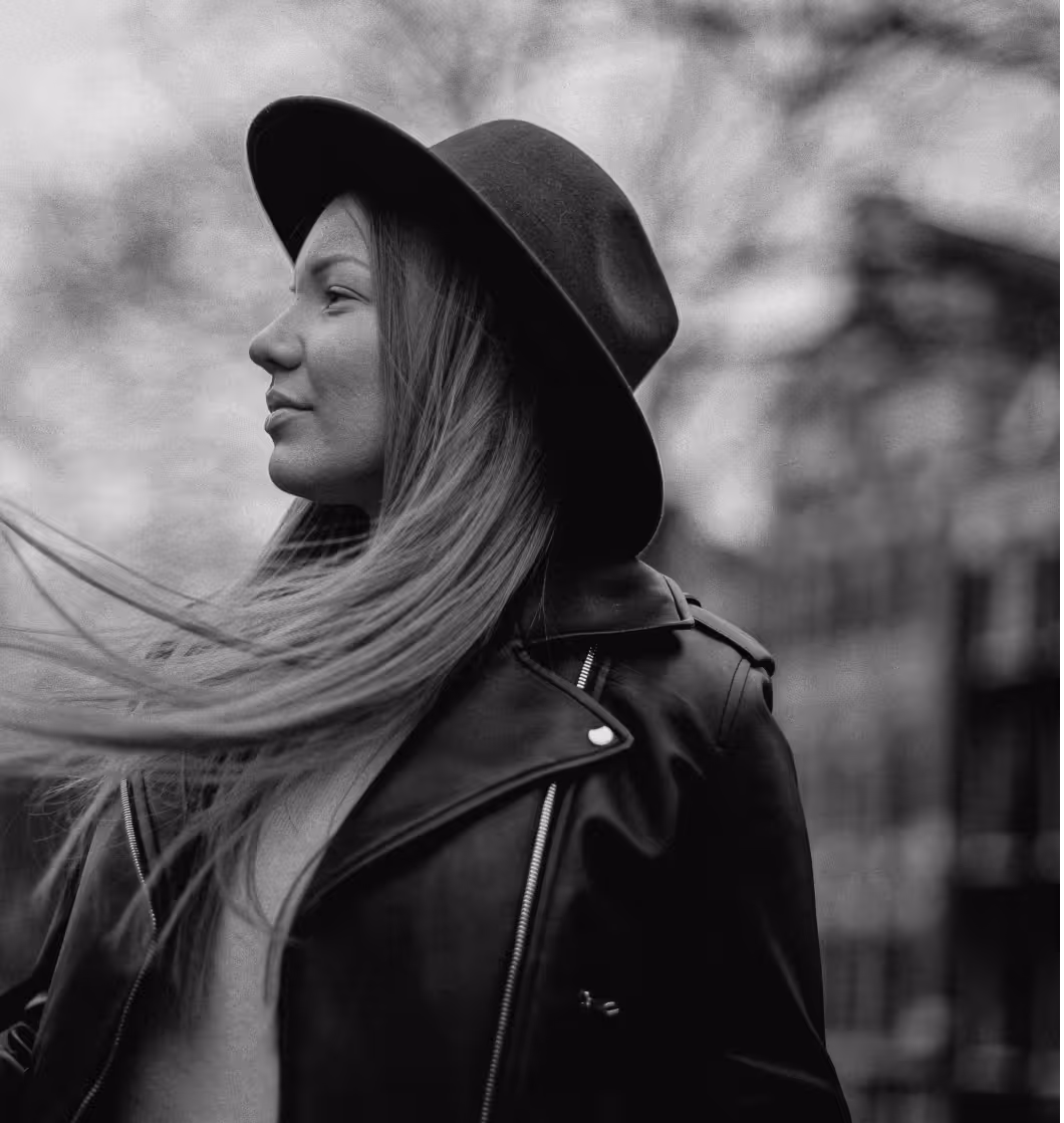 Black and white side profile of a woman wearing a hat and leather jacket with hair blowing.