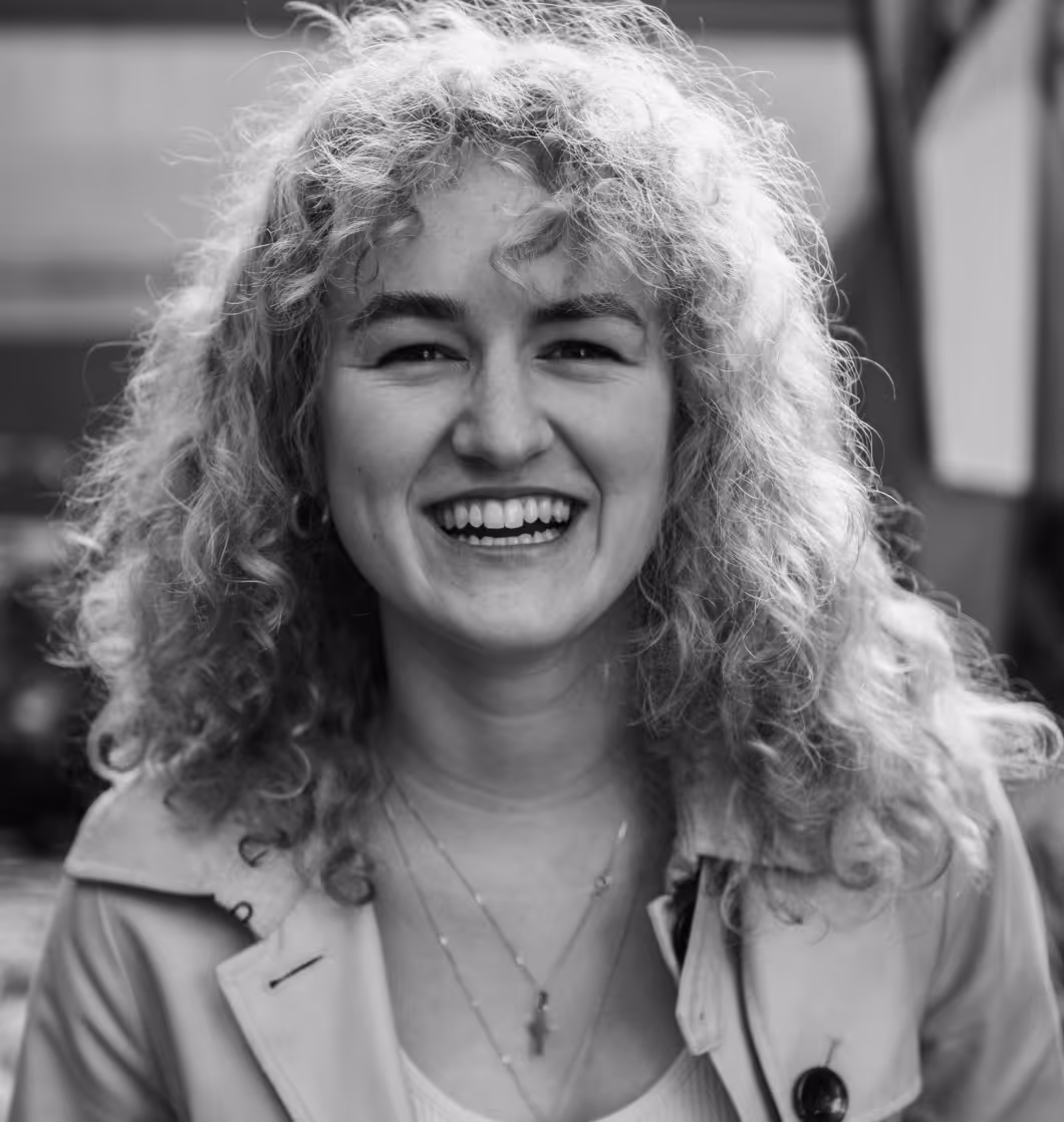 Black and white portrait of a smiling woman with curly hair and layered necklaces outdoors.