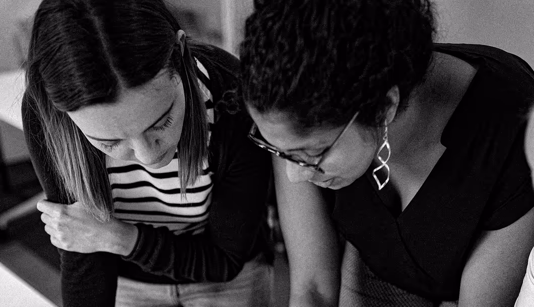 Two women leaning over a table, focused and working closely together in a collaborative setting.