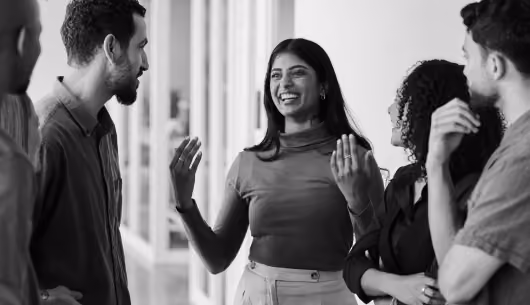 Smiling woman talking animatedly to a diverse group of people in a hallway.